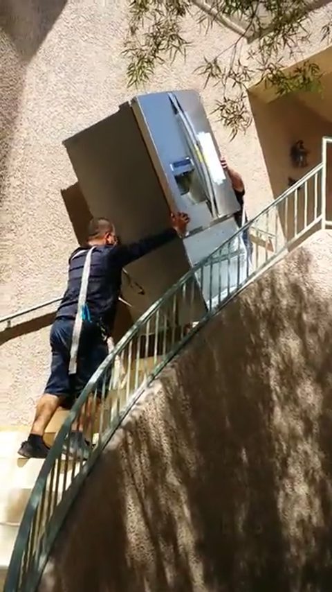 two movers carry a refrigerator up outdoor stairs to a second-floor apartment