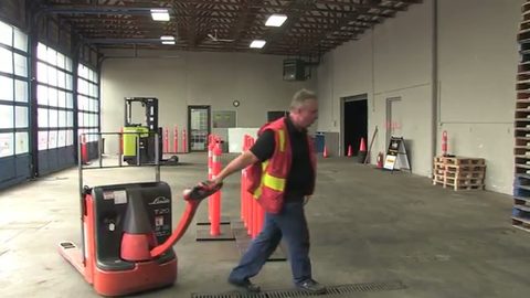 worker in a safety vest pulling an electric pallet truck, face visible