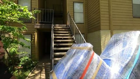 shrink-wrapped dressers at the base of an outdoor apartment staircase, face visible