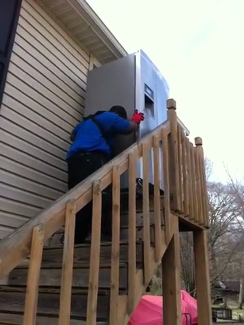 two movers moving a refrigerator onto a residential deck landing