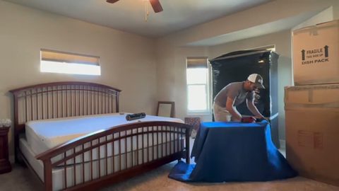 mover strapping a wrapped armoire in a bedroom, face visible