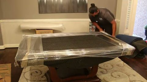 mover shrink-wrapping a blanket-wrapped dining table