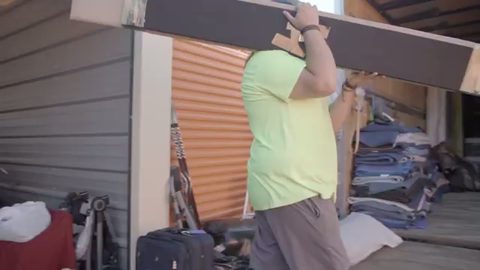 mover hoisting a long wooden bed rail on his shoulder by a storage unit