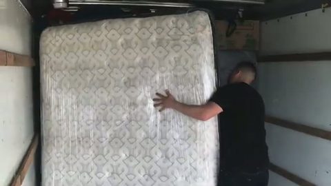 mover lifting a shrink-wrapped mattress upright in a moving truck